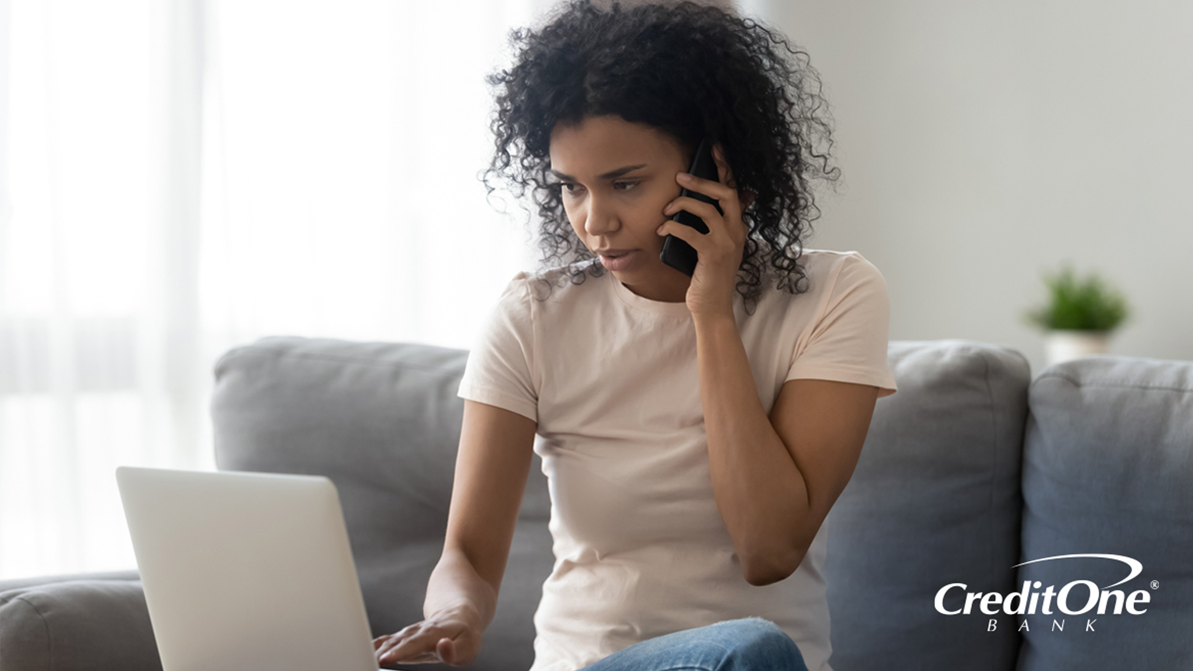 A woman looks at her laptop with a concerned expression as she talks on the phone, possibly trying to deal with a missing credit card payment.