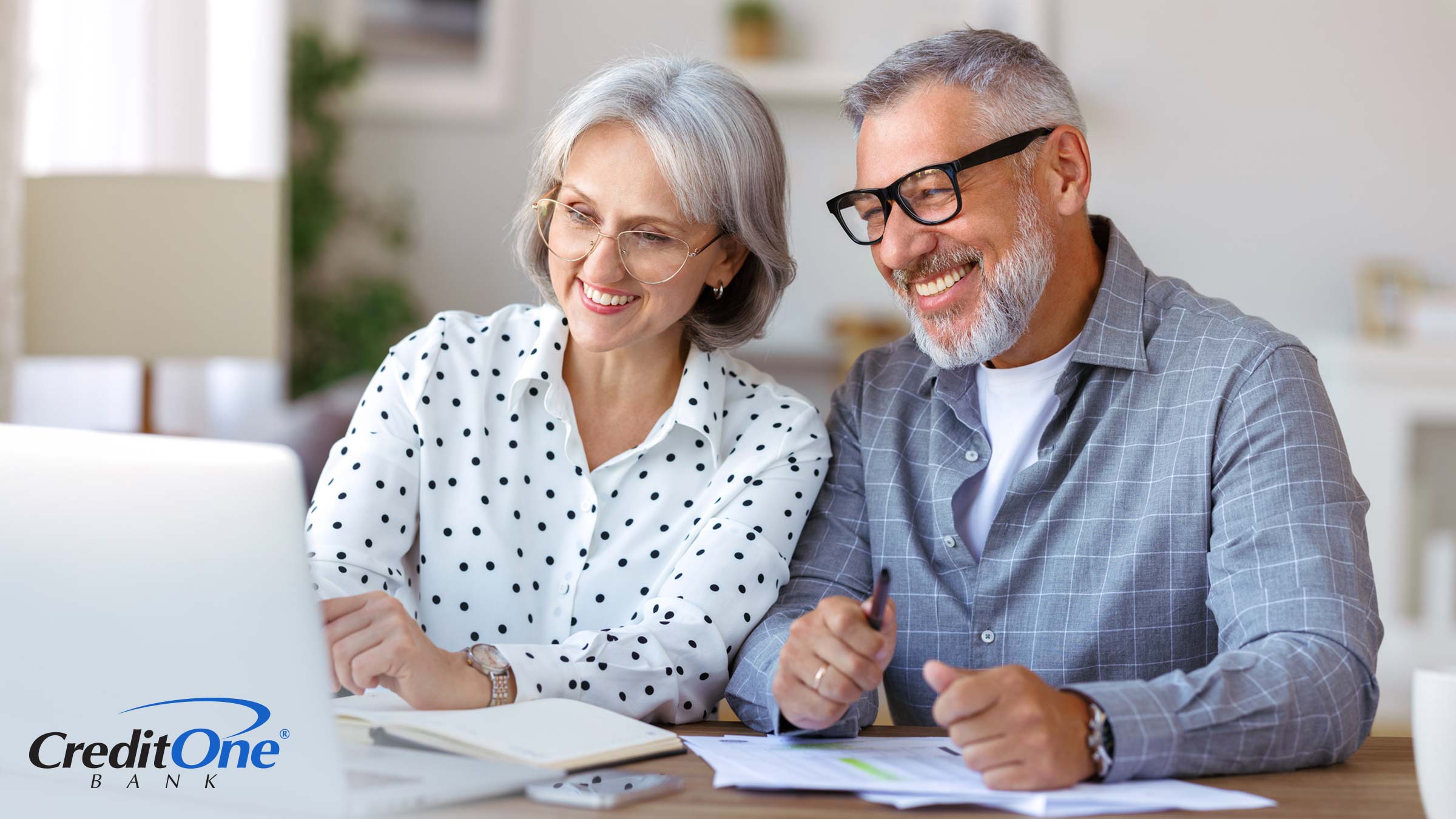 A senior couple smiles as they review their finances on a laptop, perhaps happy that jumbo CDs have proven to be a good investment.