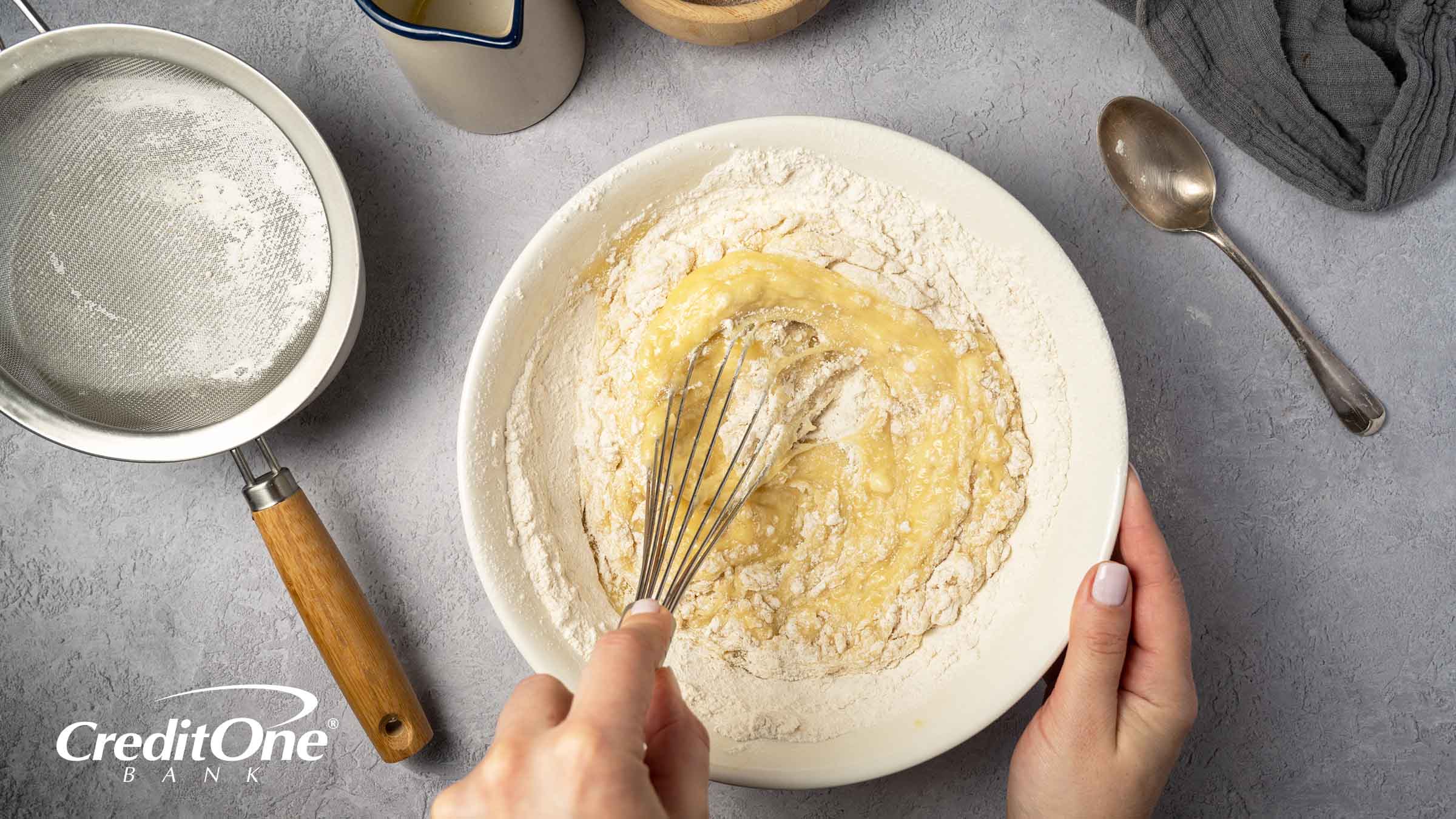 A mixing bowl with wet and dry ingredients is shown from above as the cook whisks the contents together, representing the concept of credit mix.