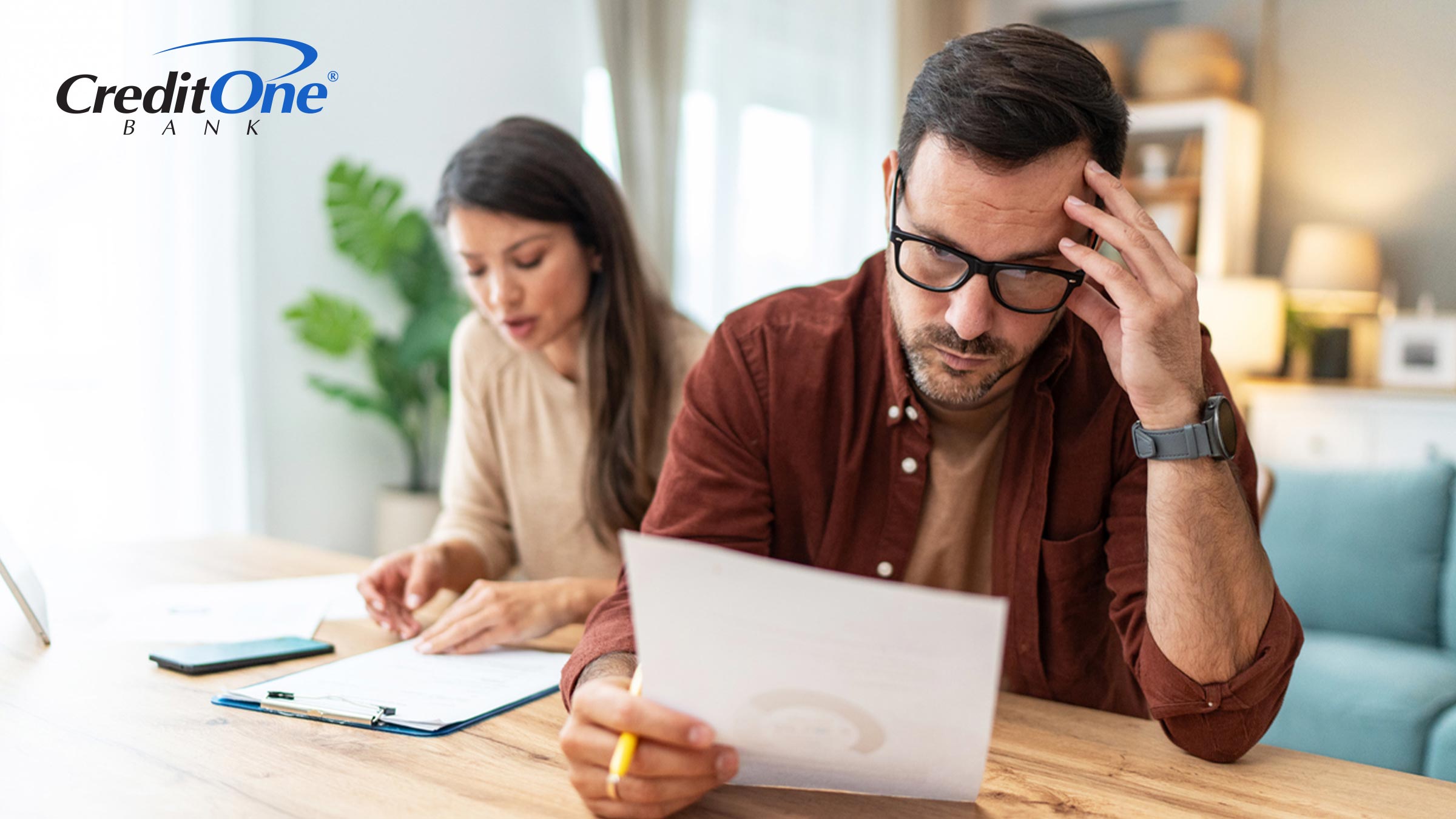 A man and woman review financial statements, with the man showing concern at a printout of a credit score. They may be dealing with the impact of an adverse credit history.