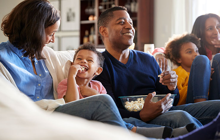 A happy family sitting on a couch eating popcorn